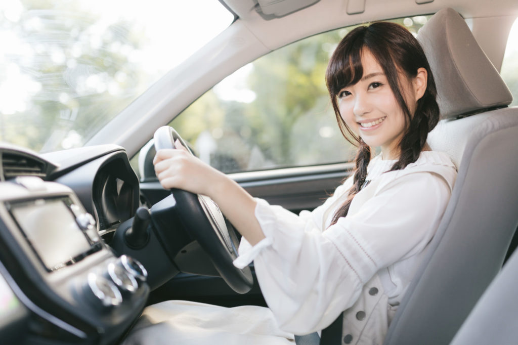 マニュアル車に乗って笑顔でMTを運転する女性ドライバー