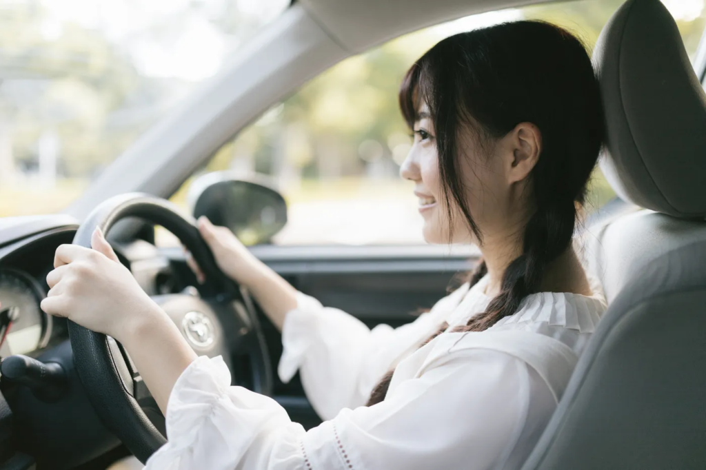 車の運転のコツを指導してもらって笑顔でハンドルを握っている女性ドライバー