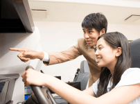 自動車学校で技能教習のシミュレーター教習を受けている女性ドライバーとインストラクター